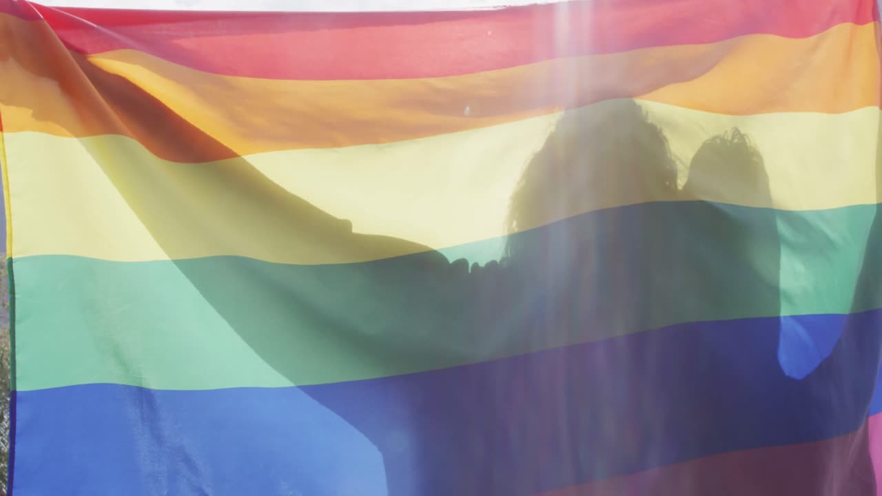 pareja masculina diversa sosteniendo juntos una bandera lgbt con los brazos abiertos