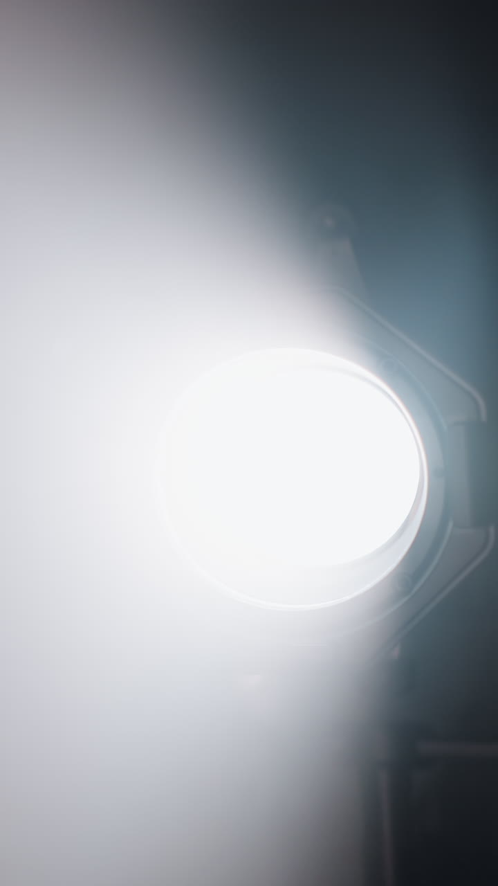 un foco de estudio intenso que brilla brillantemente en una habitación oscura, proyectando un haz de luz enfocado contra un fondo nebuloso