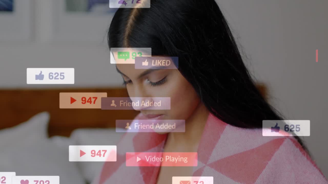 animación de iconos de redes sociales flotando sobre una mujer biracial usando un teléfono inteligente en la cama en casa.