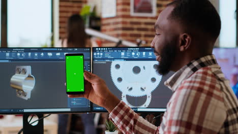 Software developer creates a gear prototype on dual monitors next to chroma key