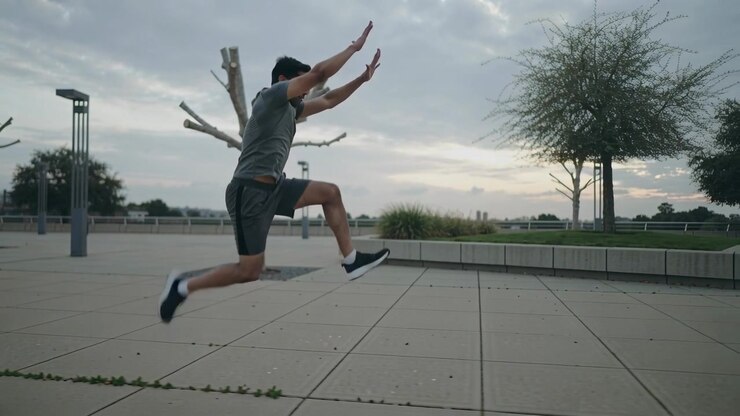 Running male athlete accelerating in grey shirt, performing forward bounds at tiled plaza training
