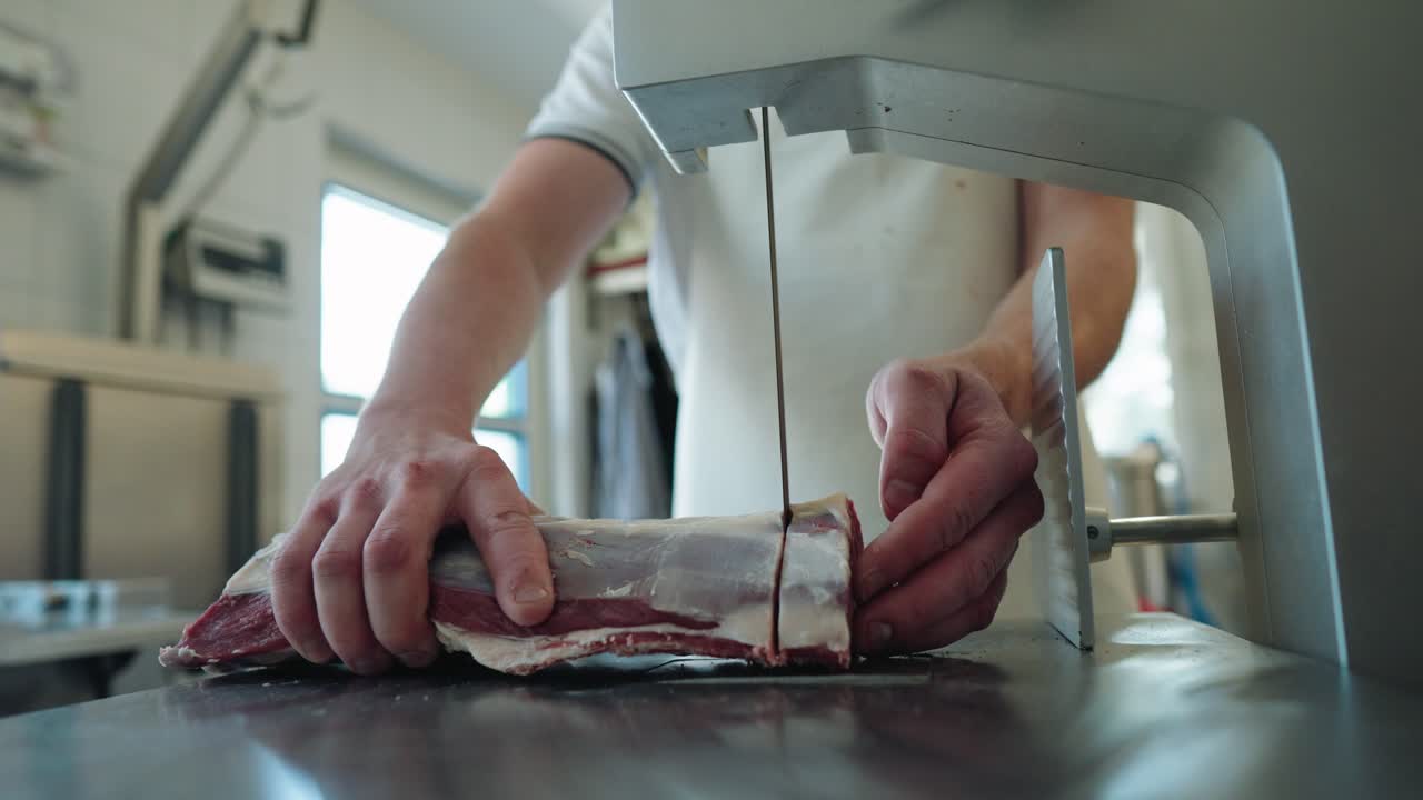 macellaio che usa la sega a nastro per tagliare le bistecche dal pezzo di agnello