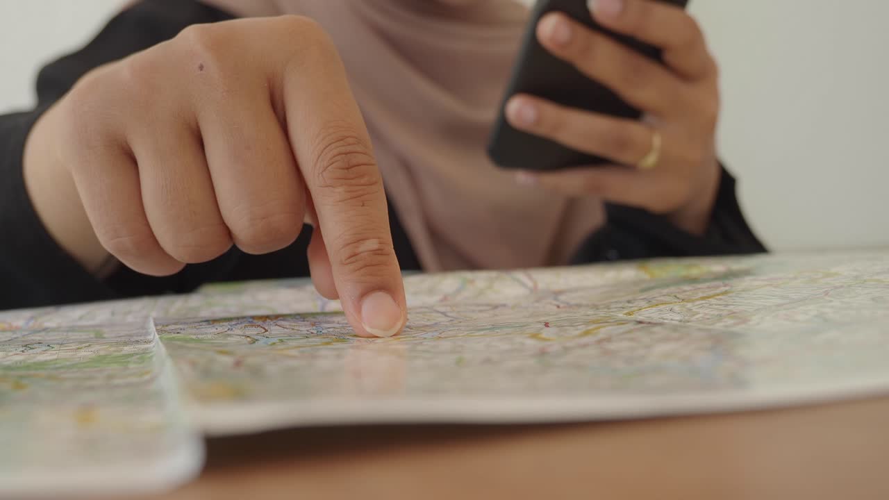 Close-up of a Person's Hand Pointing at a Map while Holding a Smartphone