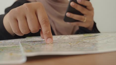 close-up of a person's hand pointing at a map while holding a smartphone