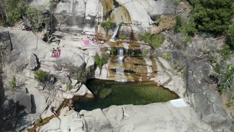 Vista-Aérea-Personas-Relajándose-En-La-Piscina-Natural-De-La-Cascada-De-Tahití-Rodeada-De-Rocas,-Gerês