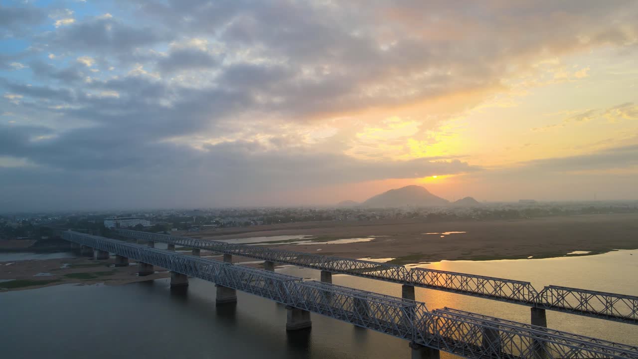 Picturesque aerial drone shot of Vijayawada at dawn, with the golden sunrise reflecting on the city’s river and buildings.