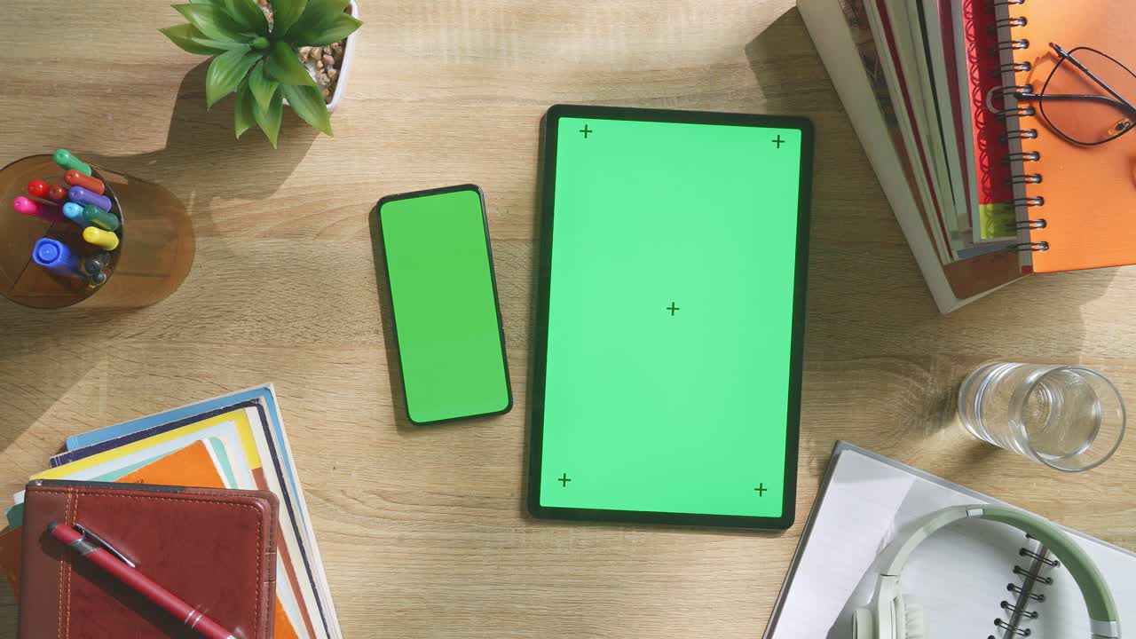vista de arriba hacia abajo de una computadora portátil con pantalla verde simulada pantalla chromakey en un escritorio de oficina de madera al lado de la libreta con bolígrafos, gafas y un vaso de agua.