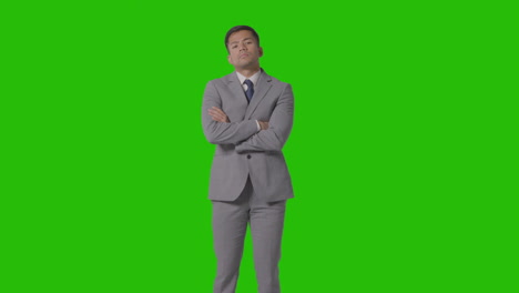 three quarter length portrait of serious businessman in suit folding arms against green screen