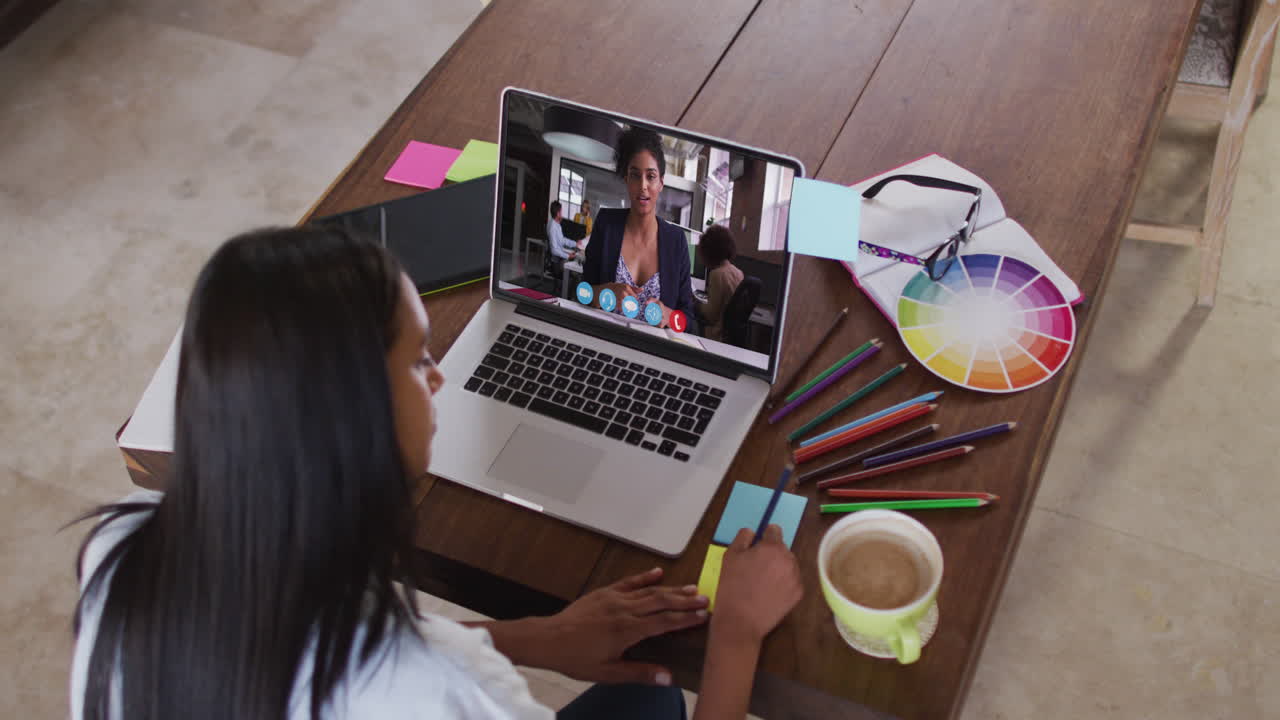mujer afroamericana escribiendo notas con una videollamada en una computadora portátil en casa