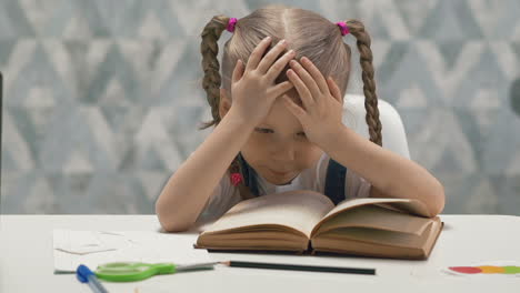 cute child with plaits tired of doing homework sits at table