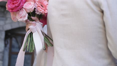 La-Novia-Sostiene-Un-Ramo-De-Boda-Rosa-Abrazando-Al-Novio-Con-Traje-Beige,-Primer-Plano-En-Cámara-Lenta