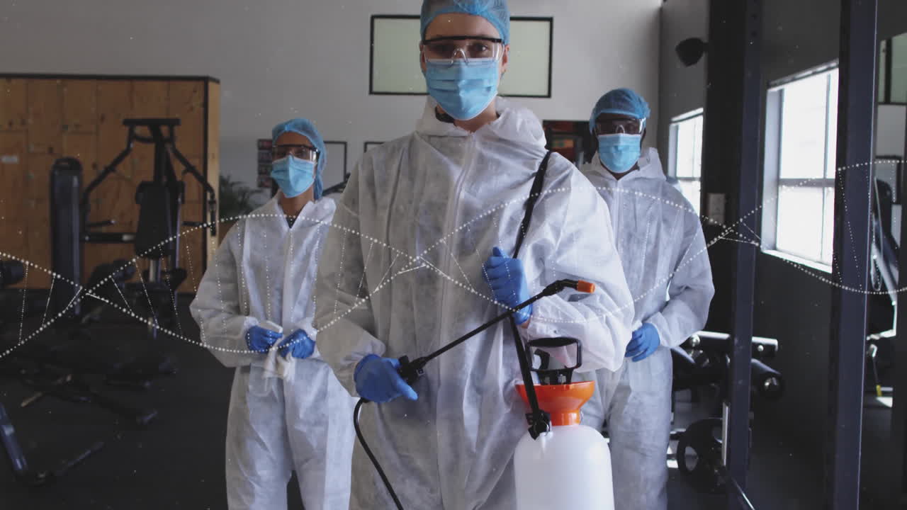 Cleaning crew wearing protective gear, spraying disinfectant in gym with animated network lines