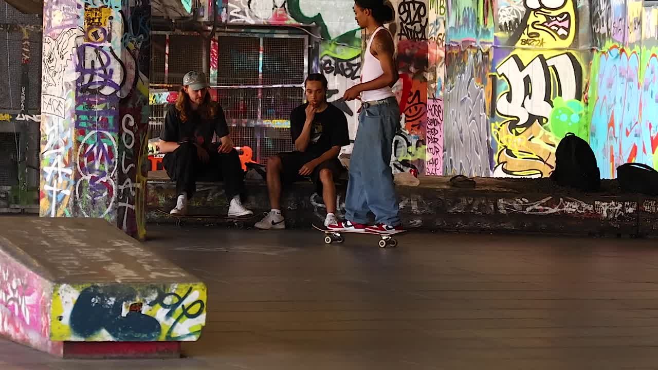 Mangfoldig gruppe unge mænd, der skater og socialiserer i en farverig, graffitifyldt urban skatepark.