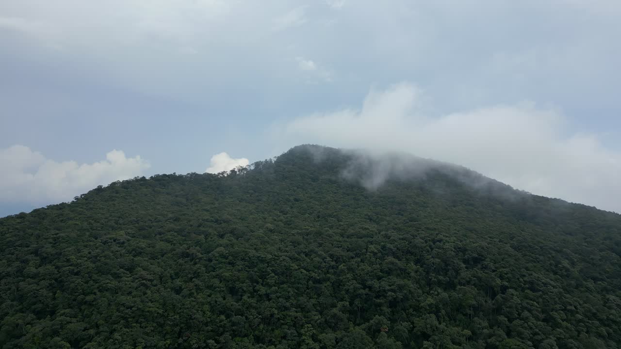 Drone flying up and over a jungle-covered peak that’s covered in fog.
