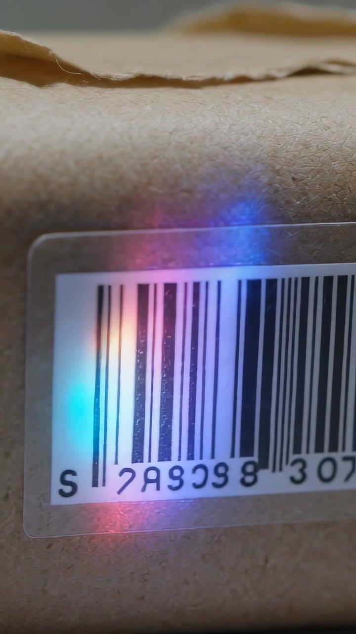 Vertical video: Appearing prism flare moving across barcode on box corner, forming rainbow hues
