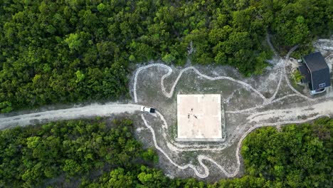 A-drone-slowly-rises-up-above-a-truck-and-three-people-lying-on-a-helicopter-pad-in-the-middle-of-a-tropical-forest-on-the-Cayman-Islands-in-the-Caribbean