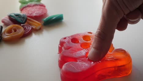 squeezing the biggest jelly bear away from other assorted gummy on a white table in studio enviroment at home