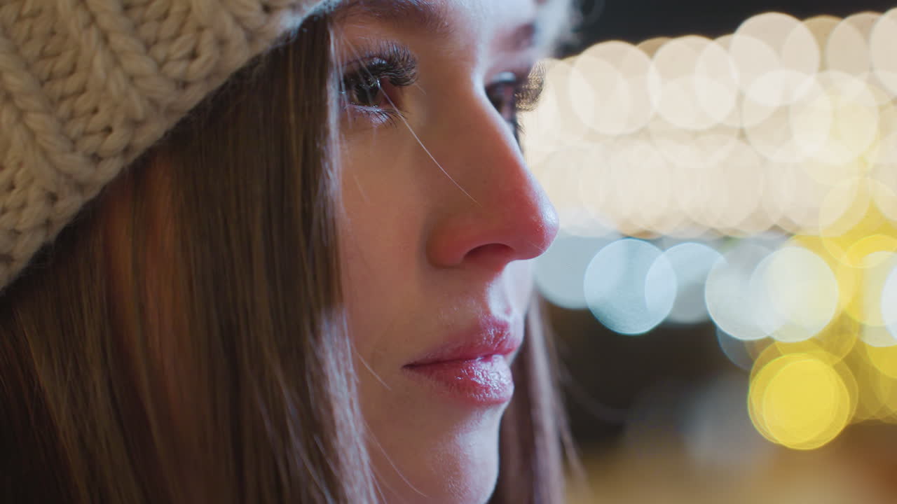 Close-up of young girl with polished nails exhaling warm breath into cold air, with visible vapor escaping, bokeh lights in background create a soft, festive atmosphere