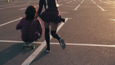 Fröhliche-Frau,-Die-Auf-Einem-Longboard-Sitzt,-Während-Ihre-Freundin-Sie-Während-Des-Sonnenuntergangs-Hinter-Sich-Herschiebt