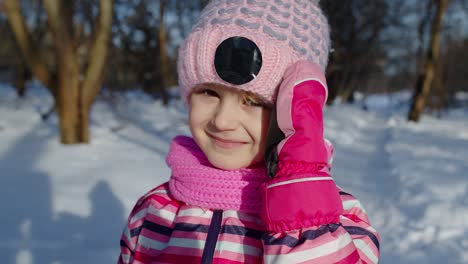 Smiling-shy-child-kid-looking-at-camera,-fooling-around,-making-faces-in-winter-snowy-park-forest