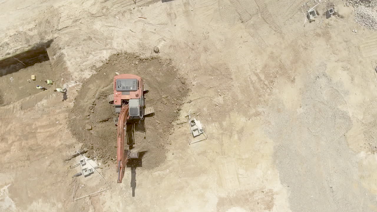 Top View Of An Excavator At Work At The Construction Site On A Sunny Day - orbiting drone shot