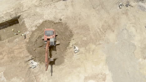 top view of an excavator at work at the construction site on a sunny day - orbiting drone shot