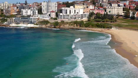 beachgoers swimming and surfing at bondi beach with oceanside swimming pool and buildings in background