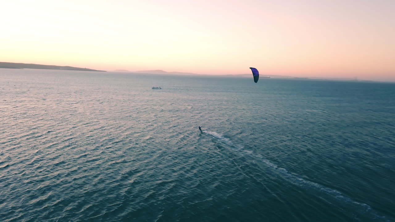 kite-surf a toda velocidad perseguido por un dron durante la puesta de sol en el océano abierto en ciudad del cabo, sudáfrica con un cielo dorado y agua azul