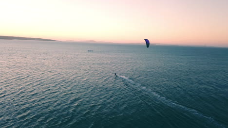 Hochgeschwindigkeits-Kitesurfer,-Der-Bei-Sonnenuntergang-Auf-Dem-Offenen-Meer-In-Kapstadt,-Südafrika,-Von-Einer-Drohne-Verfolgt-Wird,-Mit-Goldenem-Himmel-Und-Blauem-Wasser