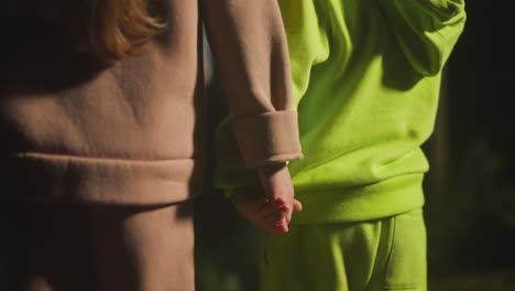 elder sister holds younger brother hand while standing in evening garden. little boy and girl dressed in comfortable sports suits spend time together having fun