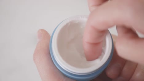 caucasian hand takes a cream from a blue plastic jar with a finger