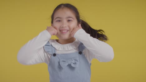 Studio-Portrait-Of-Hyperactive-Girl-Smiling-And-Pulling-Faces-Against-Yellow-Background-1