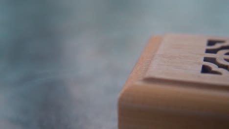 a close-up macro shot of smoking incense in a wooden box, spiritual ritual meditation, scented therapy fragrance, relaxing aromatic white smoke, textured case, smooth slowmotion video 120fps pan right