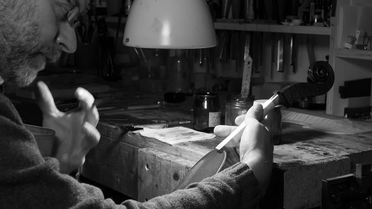 현악기 제작자가 집중 조명 아래에서 섬세한 붓놀림으로 바이올린에 광택제를 칠하고 있어요. 흑백으로 포착된 이 장면은 시간이 멈춘 듯한 작업장에서 장인 정신의 조용하지만 강렬한 모습을 슬로우 모션으로 보여줍니다.