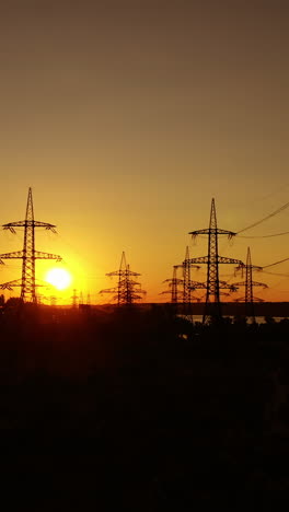 silhouette of electric towers against orange sunset. high-voltage electric lines among the evening nature. electricity efficiency. transmission lines and factory. vertical video
