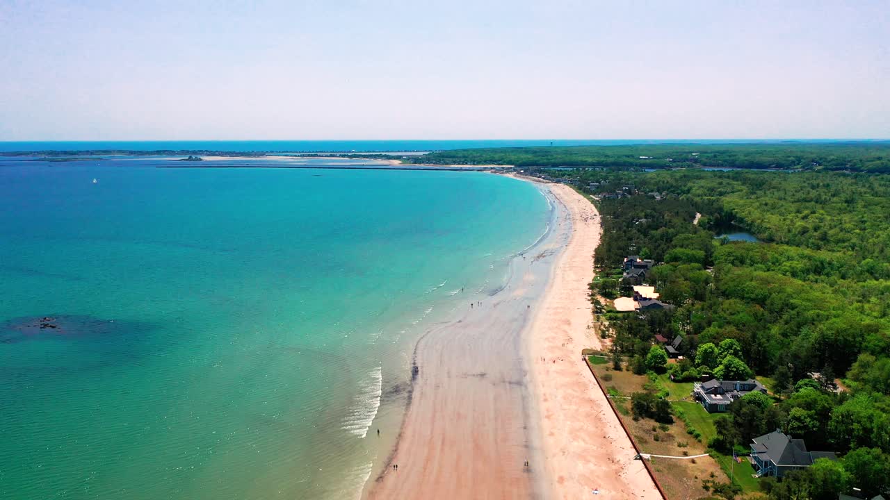 Aerial view of people-filled beaches in Saco, Maine. Vacation homes, blue waves, and families enjoying the East Coast summer. Drone shot highlights tourism, crowds, and beautiful shoreline scenery.