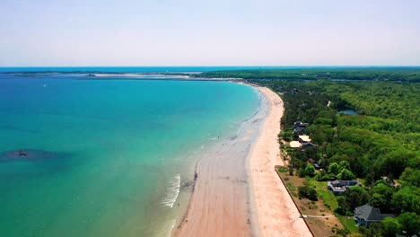 Aerial view of people-filled beaches in Saco, Maine. Vacation homes, blue waves, and families enjoying the East Coast summer. Drone shot highlights tourism, crowds, and beautiful shoreline scenery.