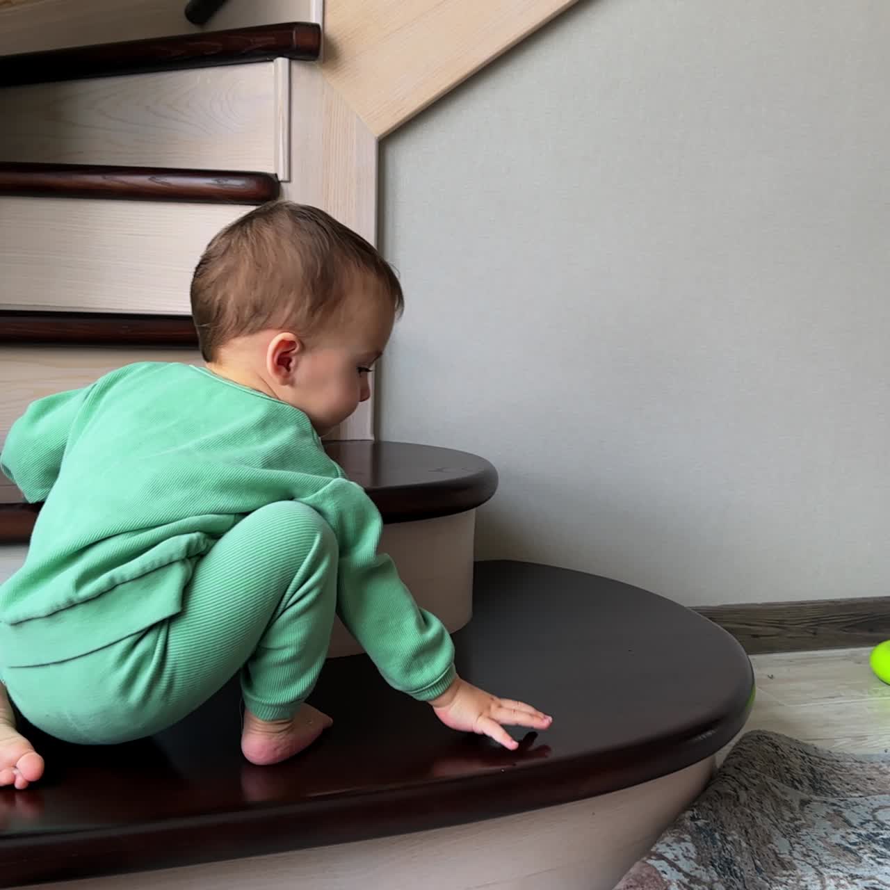 Active Caucasian baby boy climbs down the stairs to get his toy from the floor. Aimed toddler carefully puts his feet on the floor not to fall