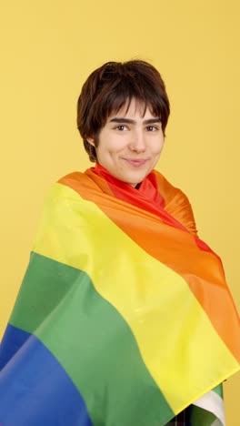person wrapped in rainbow pride flag on yellow background