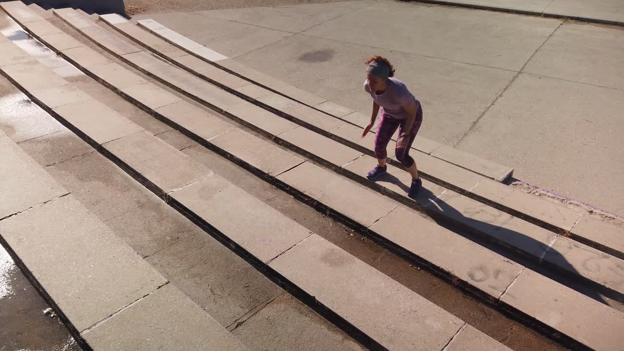 A shot focused on a redhead woman jumping some bleachers in a park