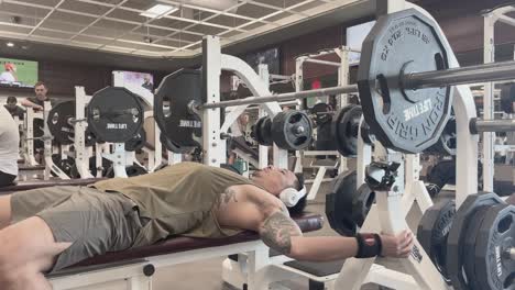 Hombre-Asiático-Con-Auriculares-Realizando-Press-De-Banca-En-El-Gimnasio.