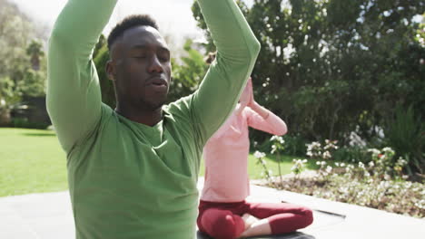 Happy-diverse-couple-exercising-yoga-in-sunny-garden,-slow-motion