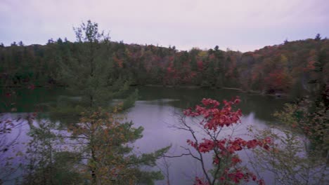 slow pan to the right over a lake on a lookout of a boardwalk with lots of autumn coloured trees on the side of the hill on either side