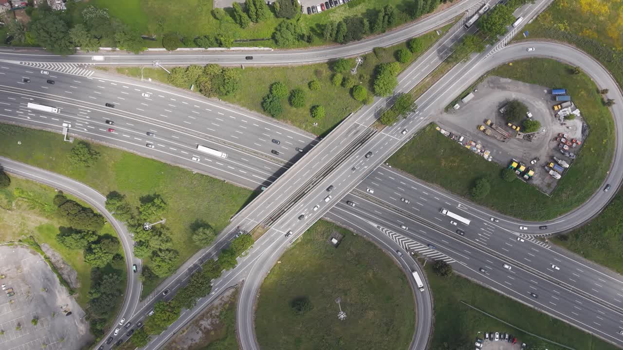 Dynamic aerial tracking shot of cars and trucks on a multi-lane highway interchange, with smooth drone motion showing traffic, infrastructure, and nearby green areas.