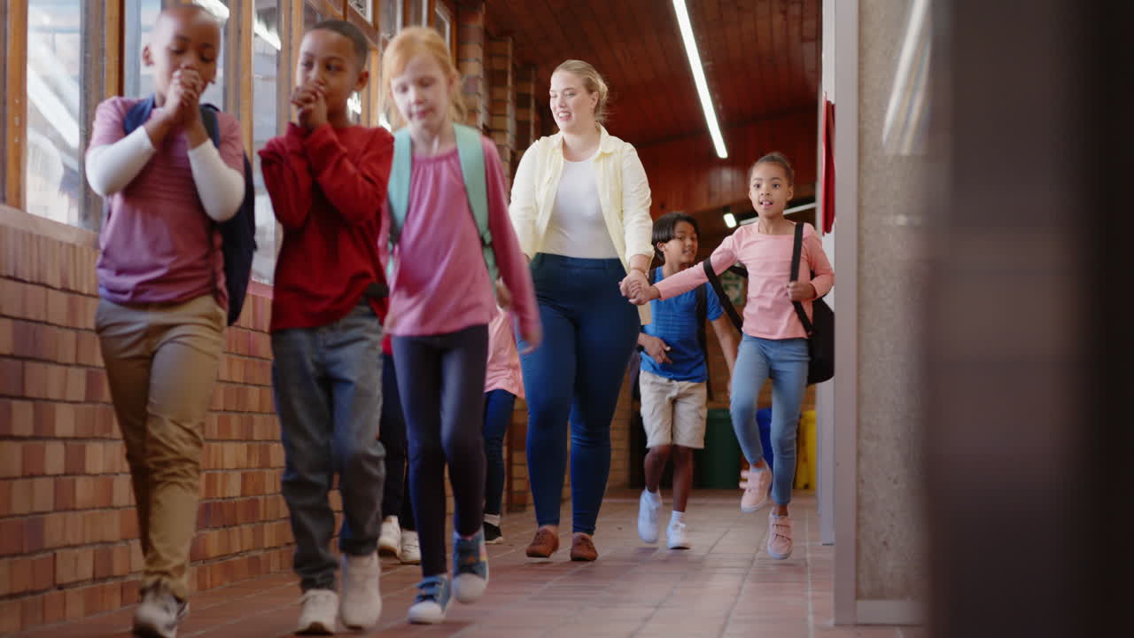Walking in school hallway, female teacher and diverse group of children holding hands