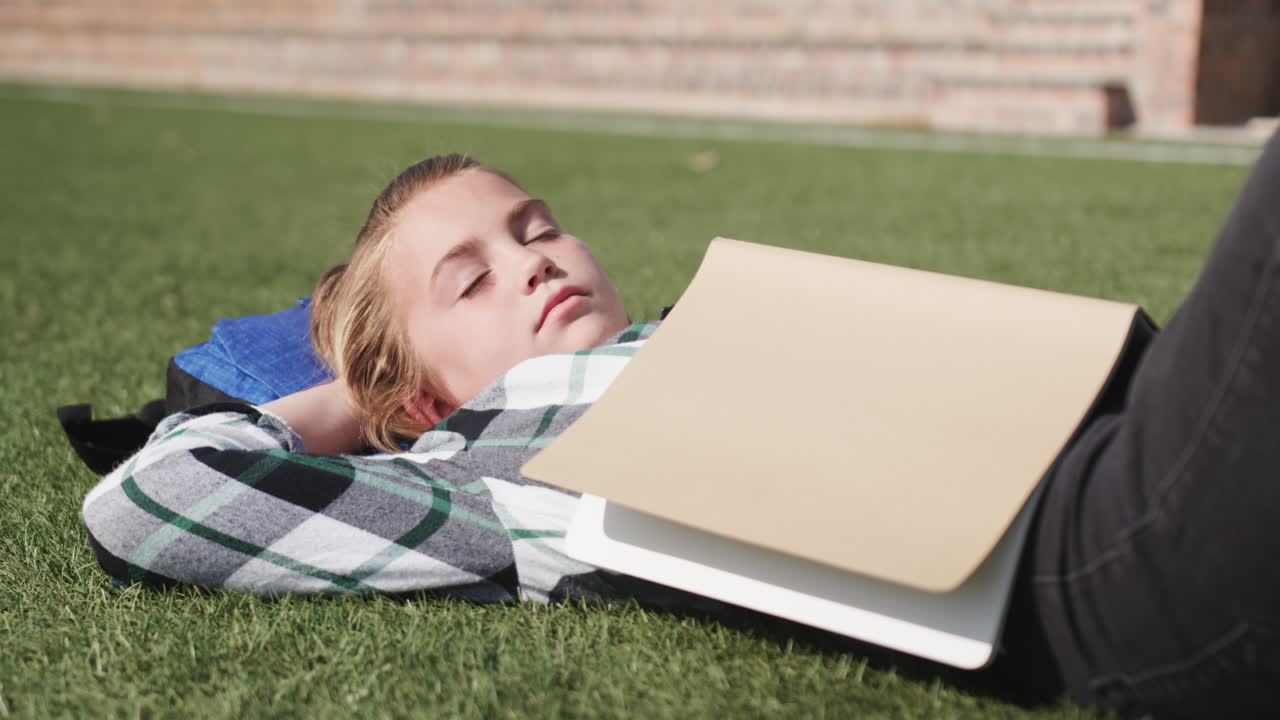 Young girl relaxing on grass with book, enjoying peaceful outdoor school break