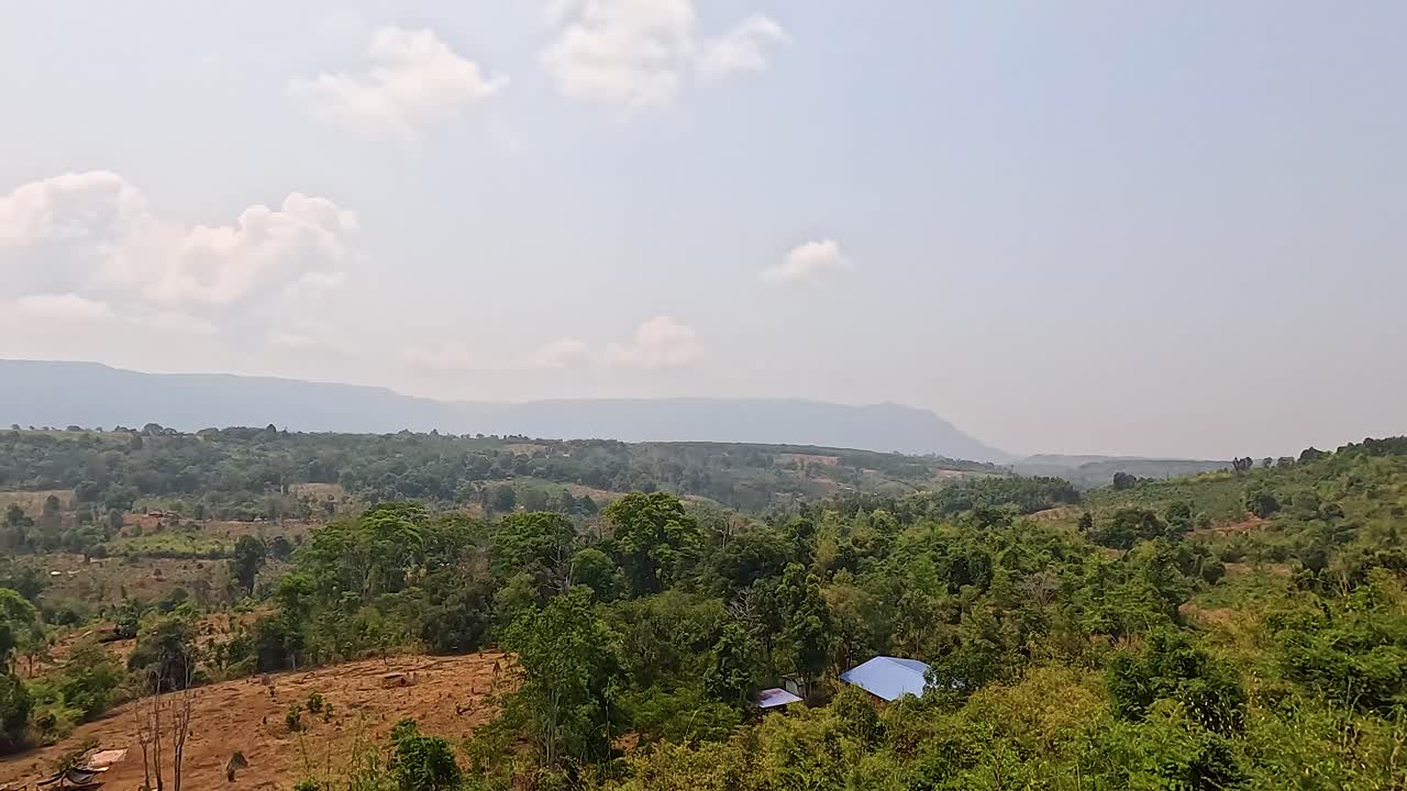 Aerial footage captures Champasak's verdant hills and expansive views under clear skies, highlighting the region's natural beauty and tranquility