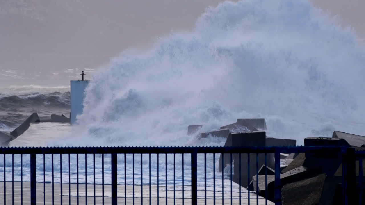 Slomo view of ocean waves crashing over dolosse and Hermanus New Harbour pier