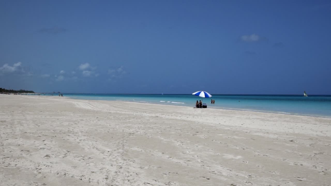 impresionante playa de varadero durante un día soleado, arena blanca y fina y mar caribe turquesa y verde, a la derecha una sombrilla azul, cuba