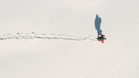 top down aerial shot of adventurous man walking through deep snow with large trekking bag